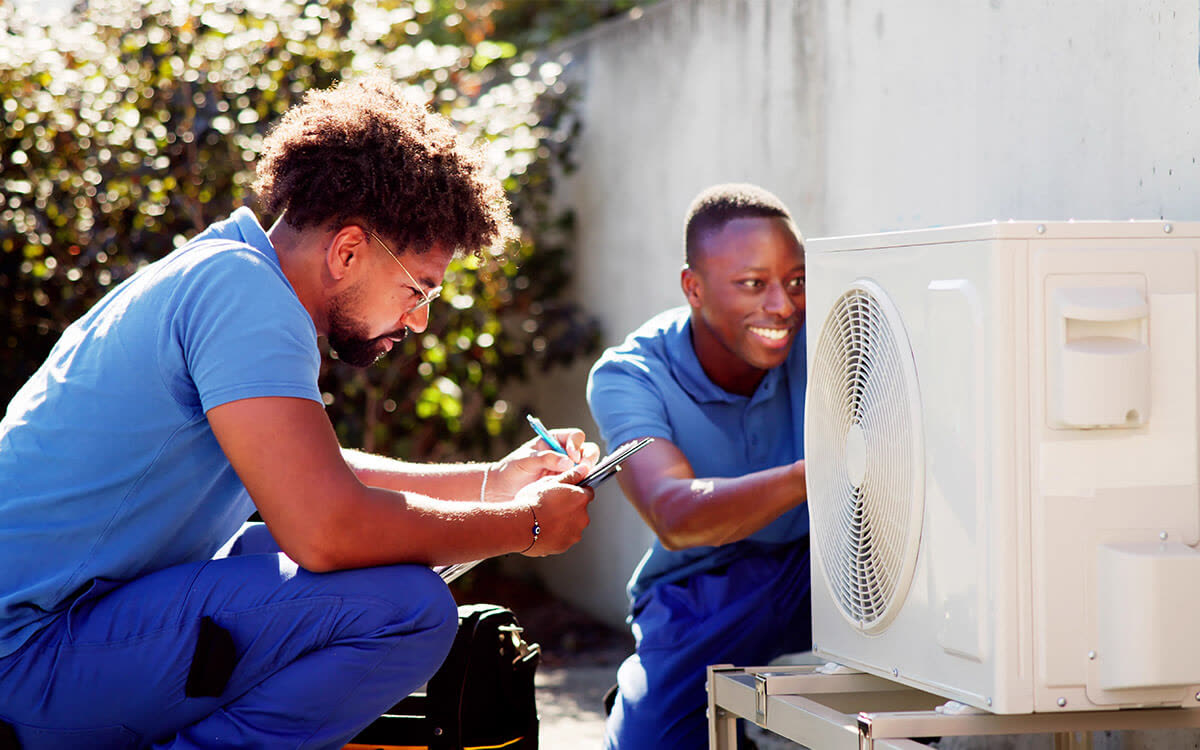 Two technicians check an outdoor air conditioning unit